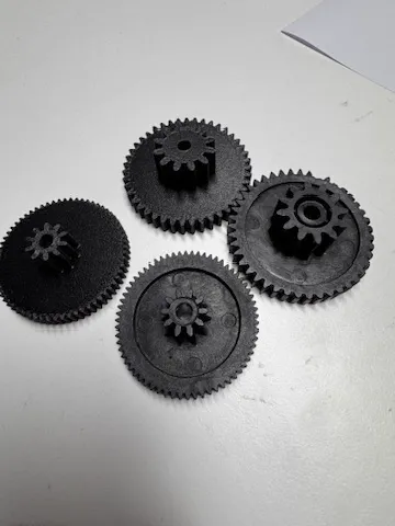 Quatre engrenages noirs imprimés en 3D, pièces de remplacement posées sur une table