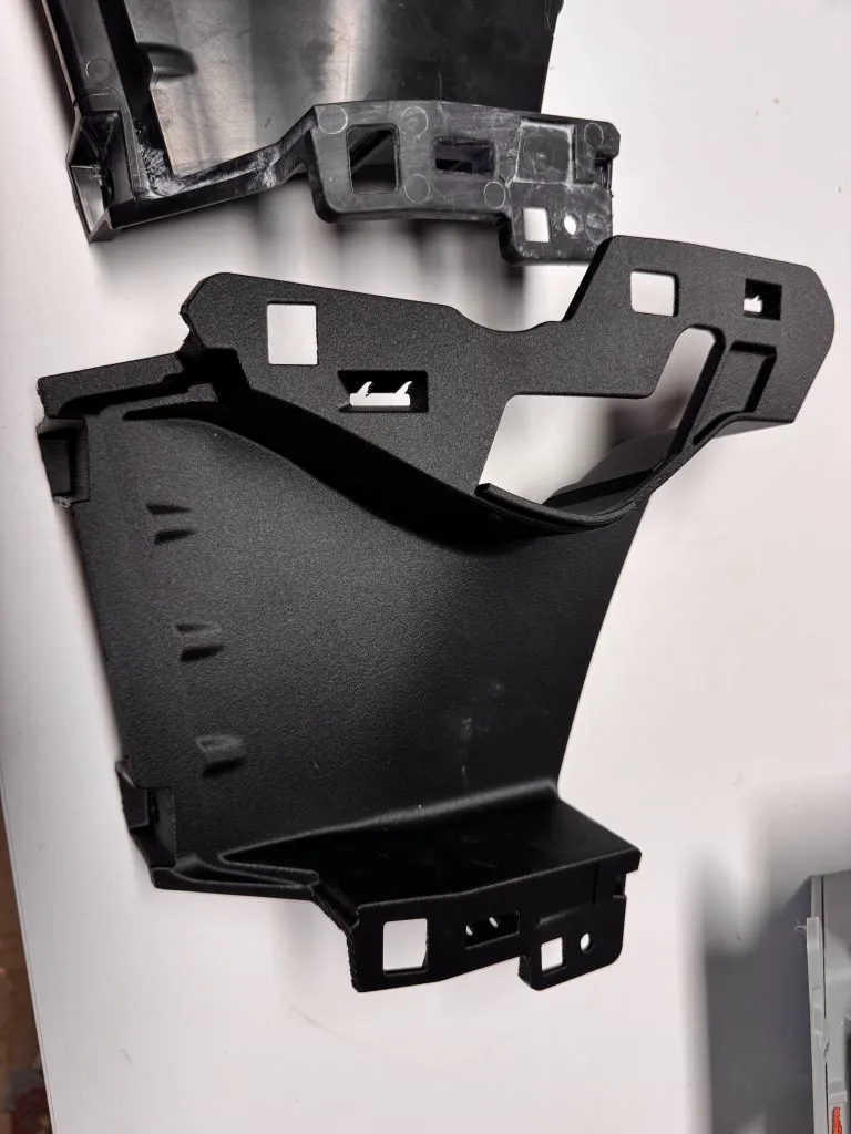 Pièce technique noire de carrosserie automobile imprimée en 3D, avec la pièce d’origine au-dessus