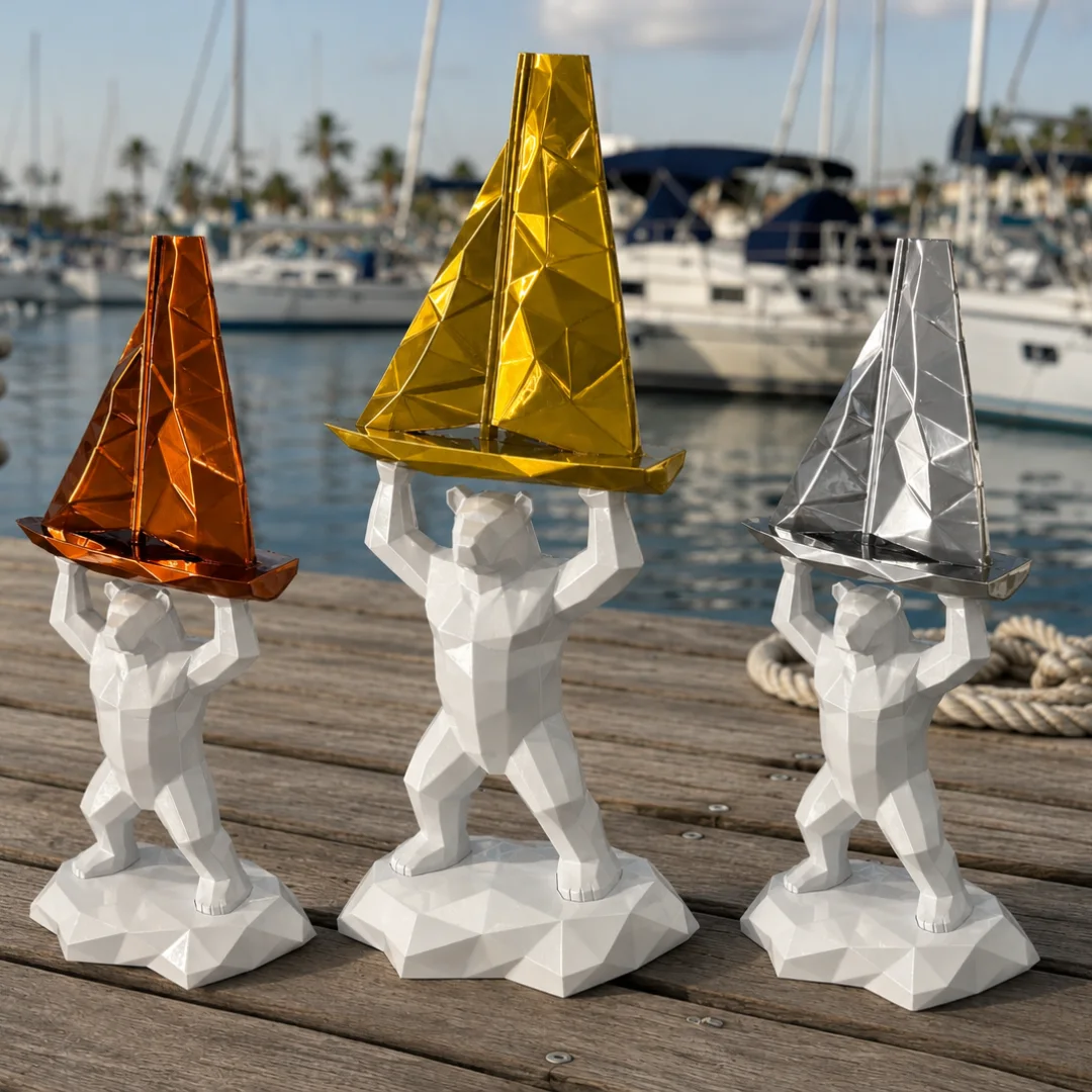Trois trophées imprimés en 3D : des ours blancs à facettes soulèvent un voilier bronze, or et argent